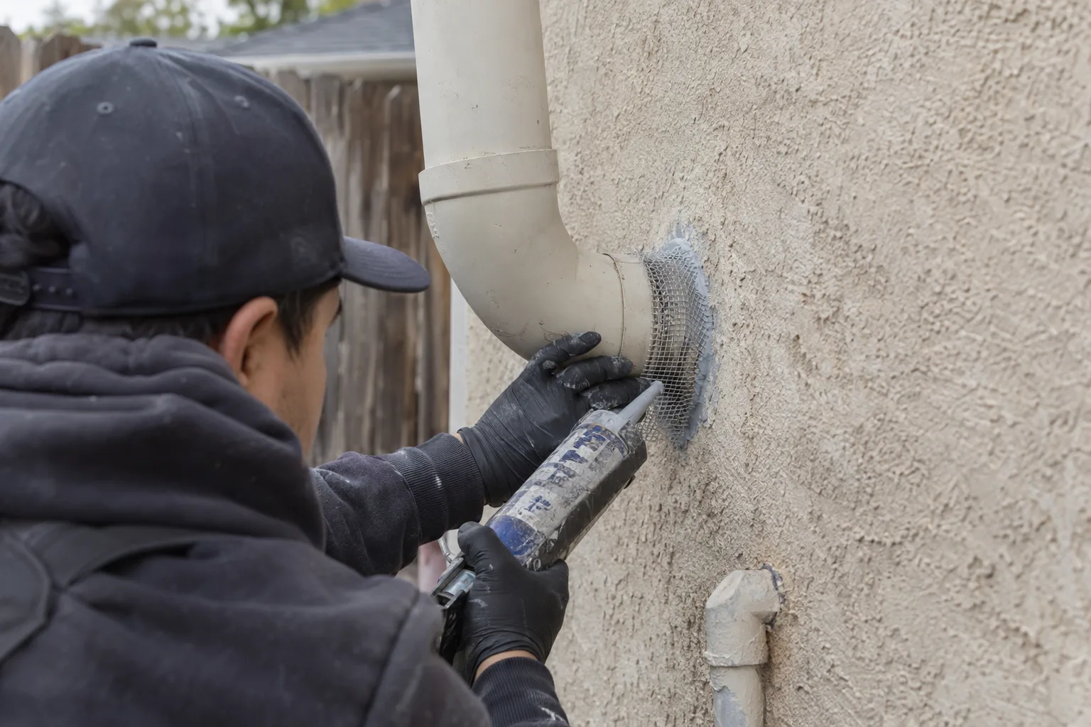 Technician sealing a pipe penetration on an exterior stucco wall