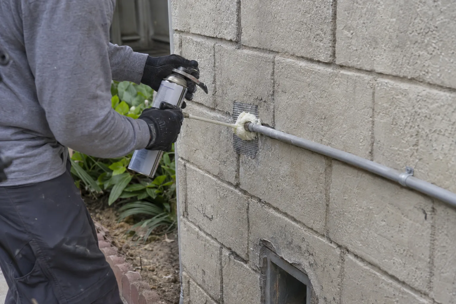 Technician sealing a gap around a utility conduit on an exterior wall